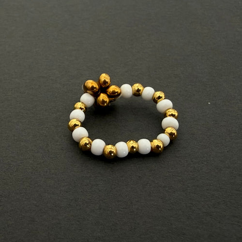 Beaded ring with gold and white beads on a dark gray background