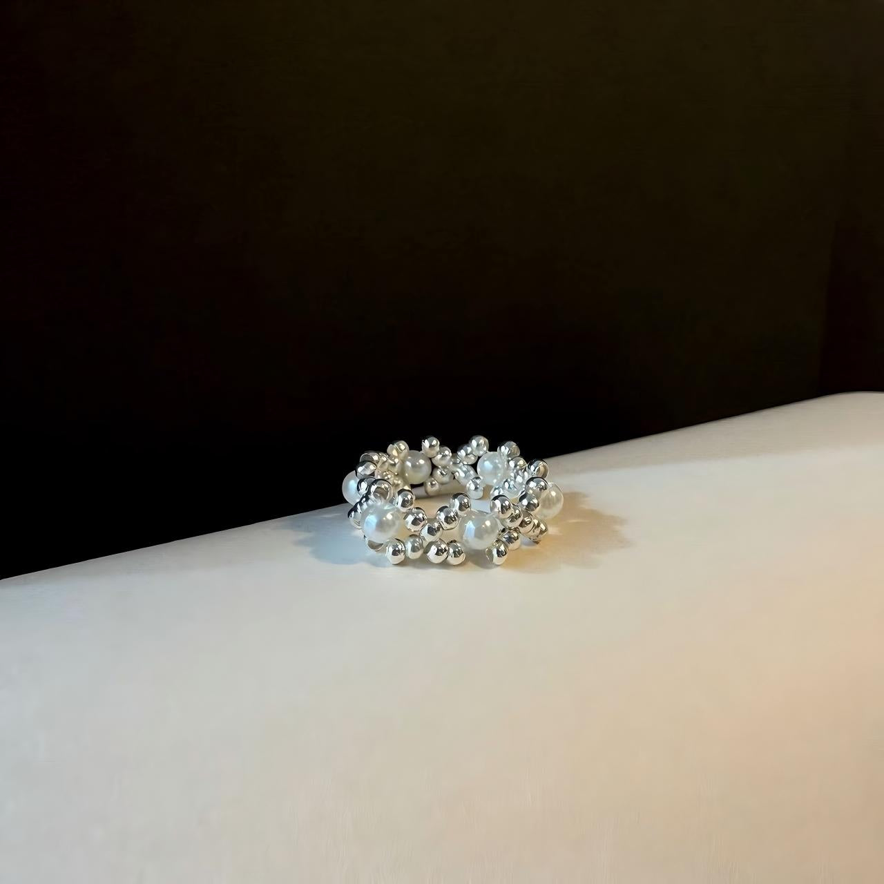 Silver beaded ring on a white surface with a black background