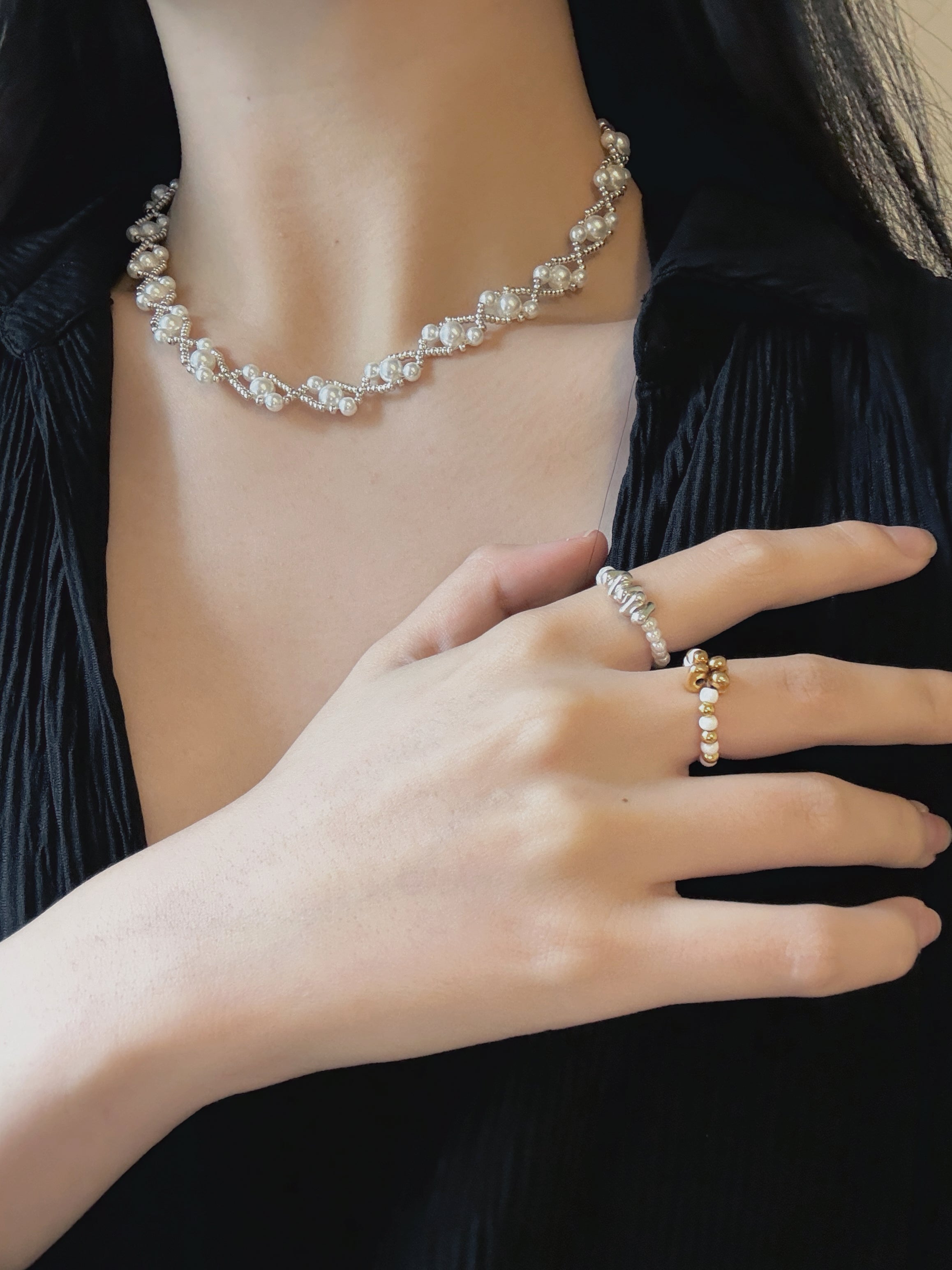 Pearl necklace and beaded rings on a person wearing a black outfit